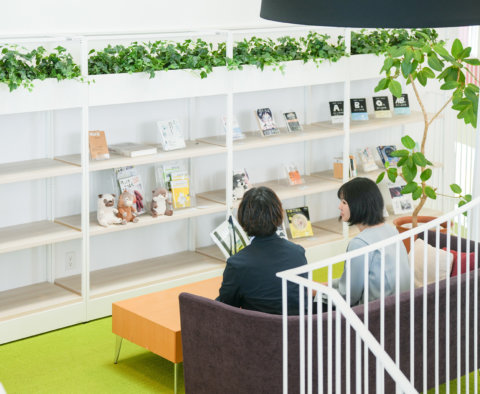 おしゃれな本棚やぬいぐるみがある図書スペースのソファに座り、落ち着いて会話をする2人の男女。吹き抜けの上から見下ろすアングル。