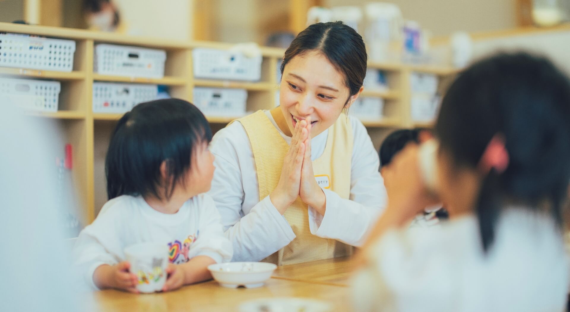子どもたちの食事のお世話をする女性保育士の写真