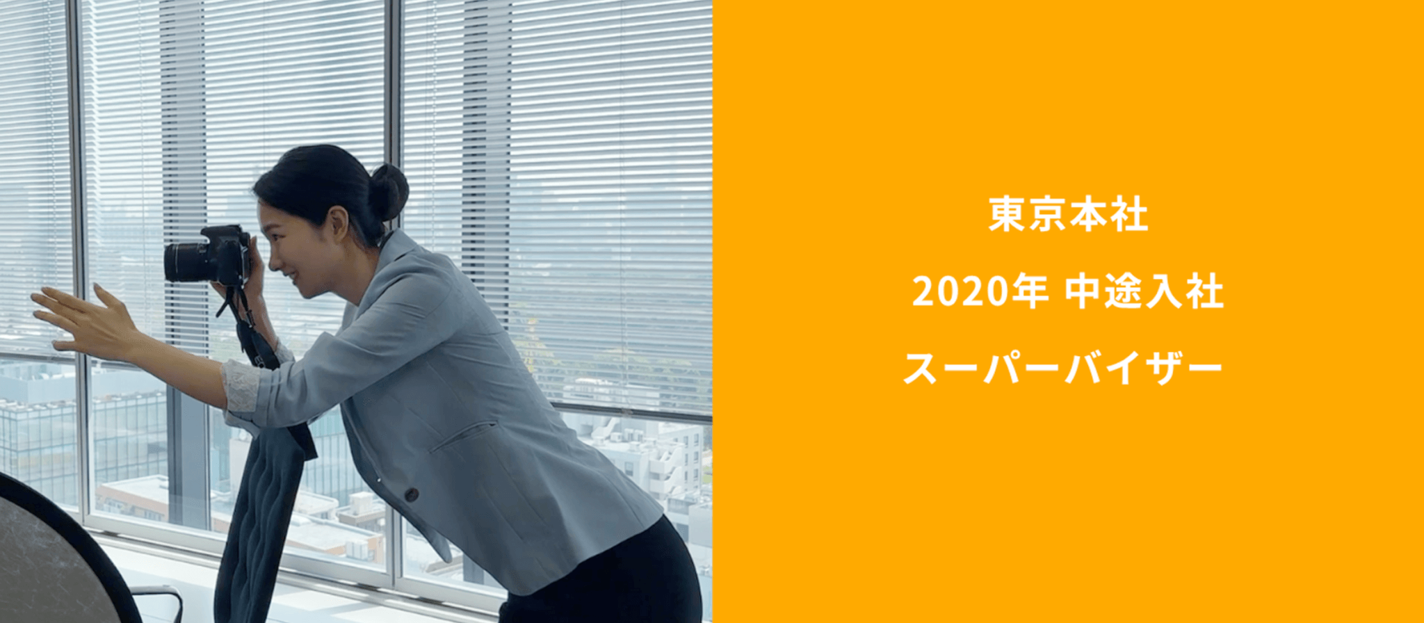 オフィスでカメラを構える女性。右側のオレンジ色の背景に「東京本社 2020年 中途入社 スーパーバイザー」というテキストが記載されている。