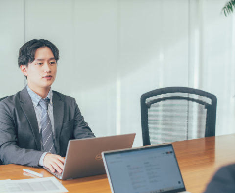 オフィスでスーツ姿の男性がノートパソコンの前で真剣に打ち合わせをしている様子