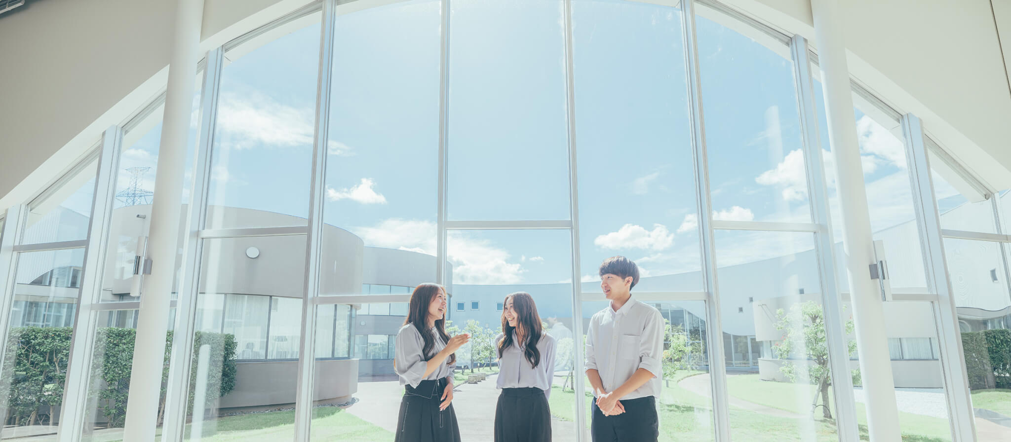 明るいガラス張りの空間で、笑顔でコミュニケーションをとる男女3人組