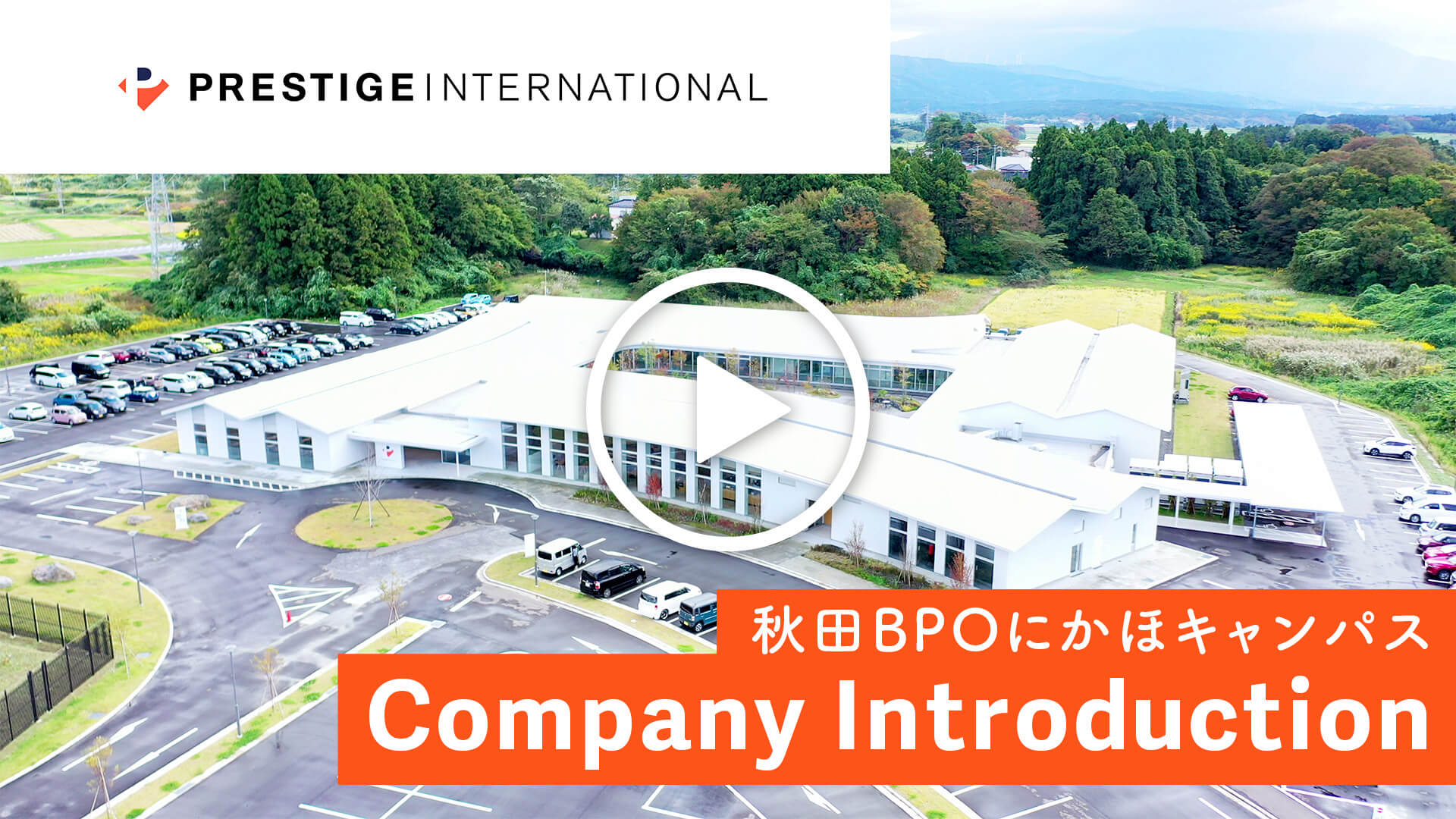 プレステージ・インターナショナル 秋田BPOにかほキャンパスの全景。豊かな自然に囲まれた白い平屋建てのオフィスビルと駐車場の空撮写真。右下に「Company Introduction」の文字。