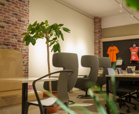 レンガ調の壁がおしゃれなオフィス休憩室。スポーツチームのユニフォームが飾られ、特徴的なデザインの椅子や観葉植物が配置されたモダンな内装。